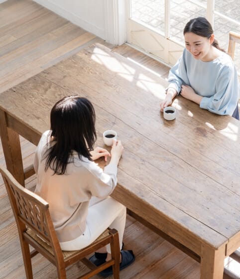 ダイニングテーブルに向き割って笑顔で話す二人の女性